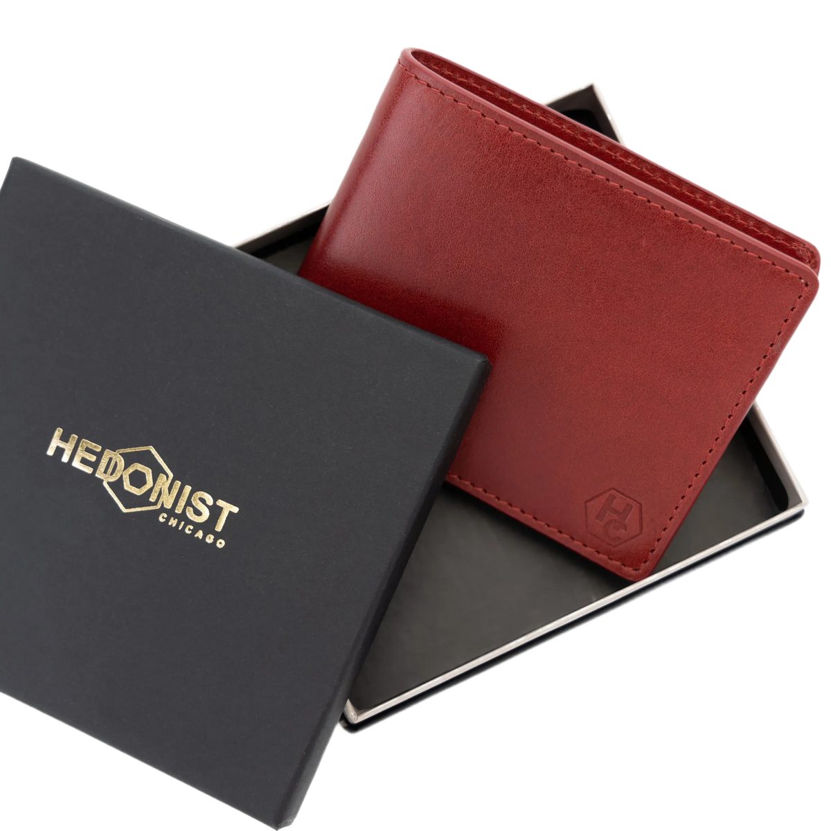 A red leather bi-fold wallet displayed in an open black presentation box with a matching branded lid. The lid shows the gold-toned HEDONIST CHICAGO logo.