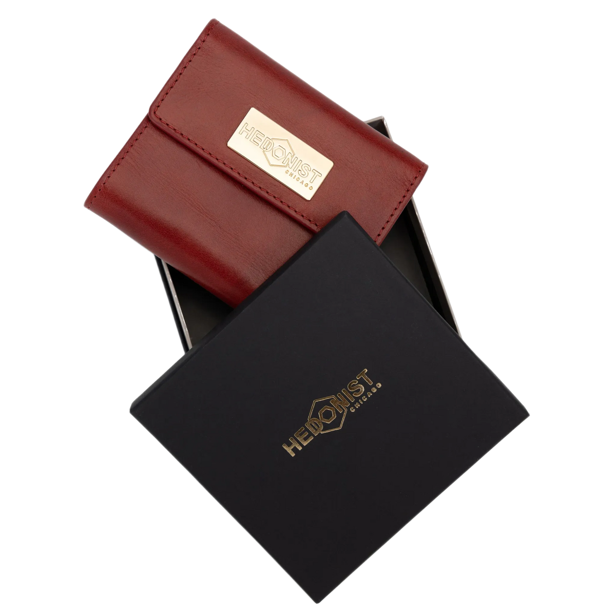 A red leather wallet with a gold-tone logo plaque, shown partially inside a black presentation box with a matching gold HEDONIST logo.