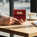 Red wallet with a brand logo held by hands on a wooden table with a blurred background
