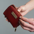 A close-up of a person's hands holding an open red leather wallet with gold-tone hardware 