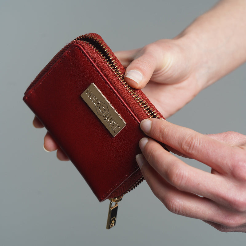 A close-up of a person's hands holding an open red leather wallet with gold-tone hardware 